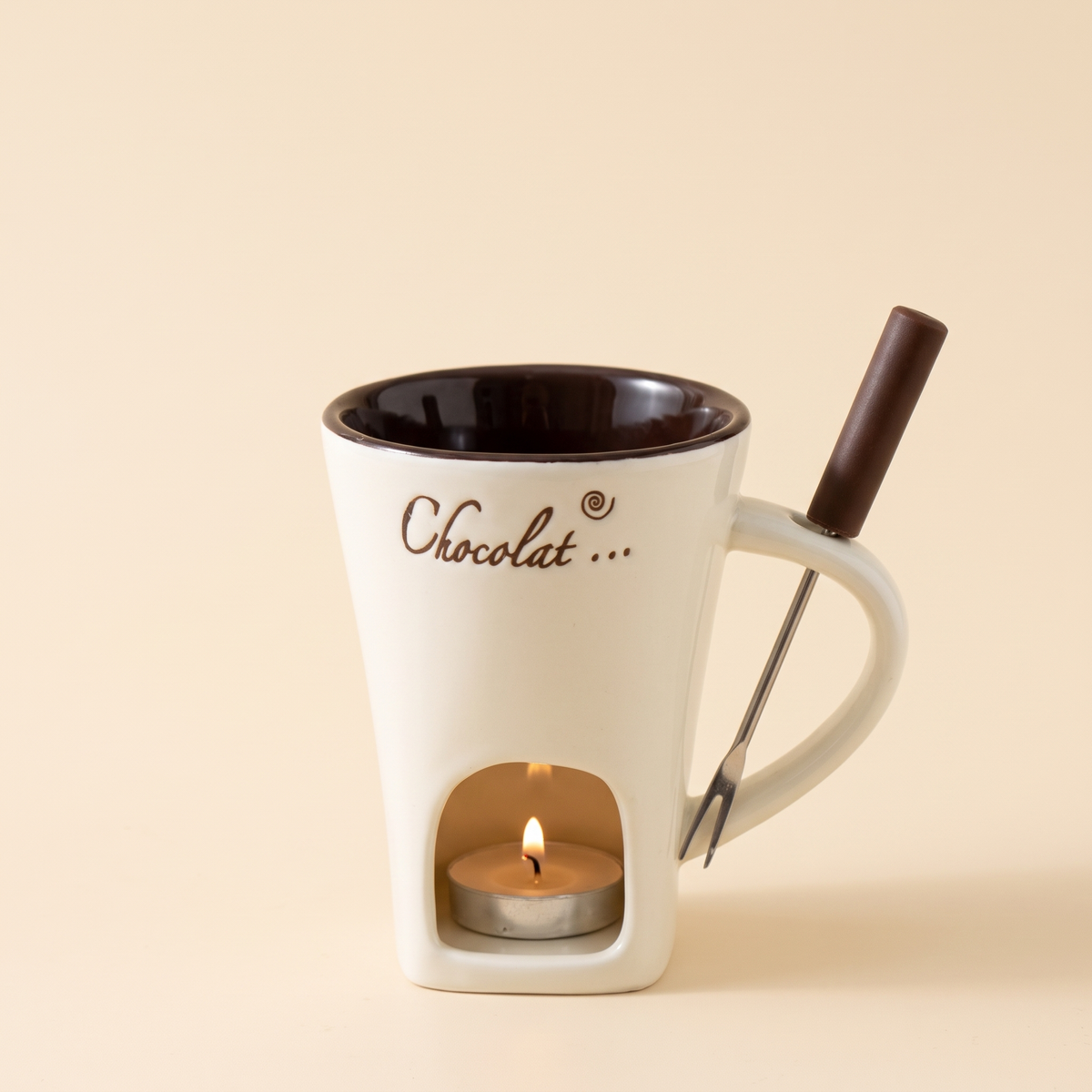 Mini-Fondue-Tasse in Beige mit dunkelbrauner Innenseite, freigestellt auf cremefarbenem Hintergrund, mit Fondue-Gabel im Henkel und brennendem Teelicht