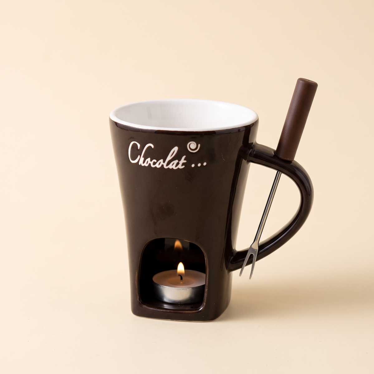 Mini-Fondue-Tasse in Schokobraun freigestellt auf cremefarbenem Hintergrund, mit Fondue-Gabel im Henkel und brennendem Teelicht